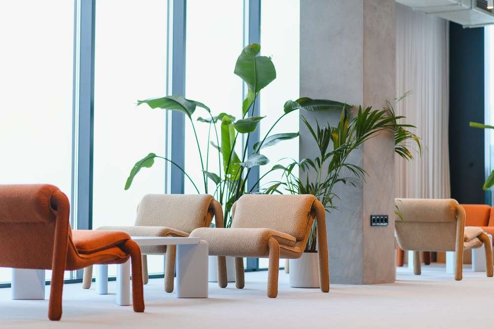 Contemporary lounge area in a corporate building featuring stylish armchairs, minimalist tables, and lush green indoor plants creating a relaxing space